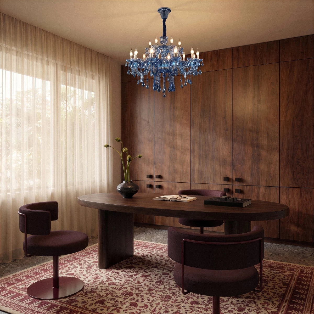Clérachic blue crystal chandelier lit above an oval walnut desk with two plum swivel chairs in a wood-panelled study
