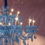 Close view of Clérachic blue glass arms, cut-glass cups and warm candle bulbs against a plum wall