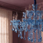 Close view of Clérachic blue chandelier candle bulbs, glass arms and teardrop crystals beside a lace curtain