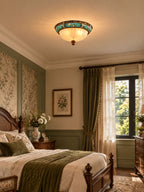 Clérachic ceiling light above a bedroom with floral wall panels, a green throw on a wooden bed and a sheer-curtained window.