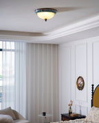 Small Clérachic ceiling light on a white ceiling with moulding, above a bedroom with sheer curtains and a panelled wall.