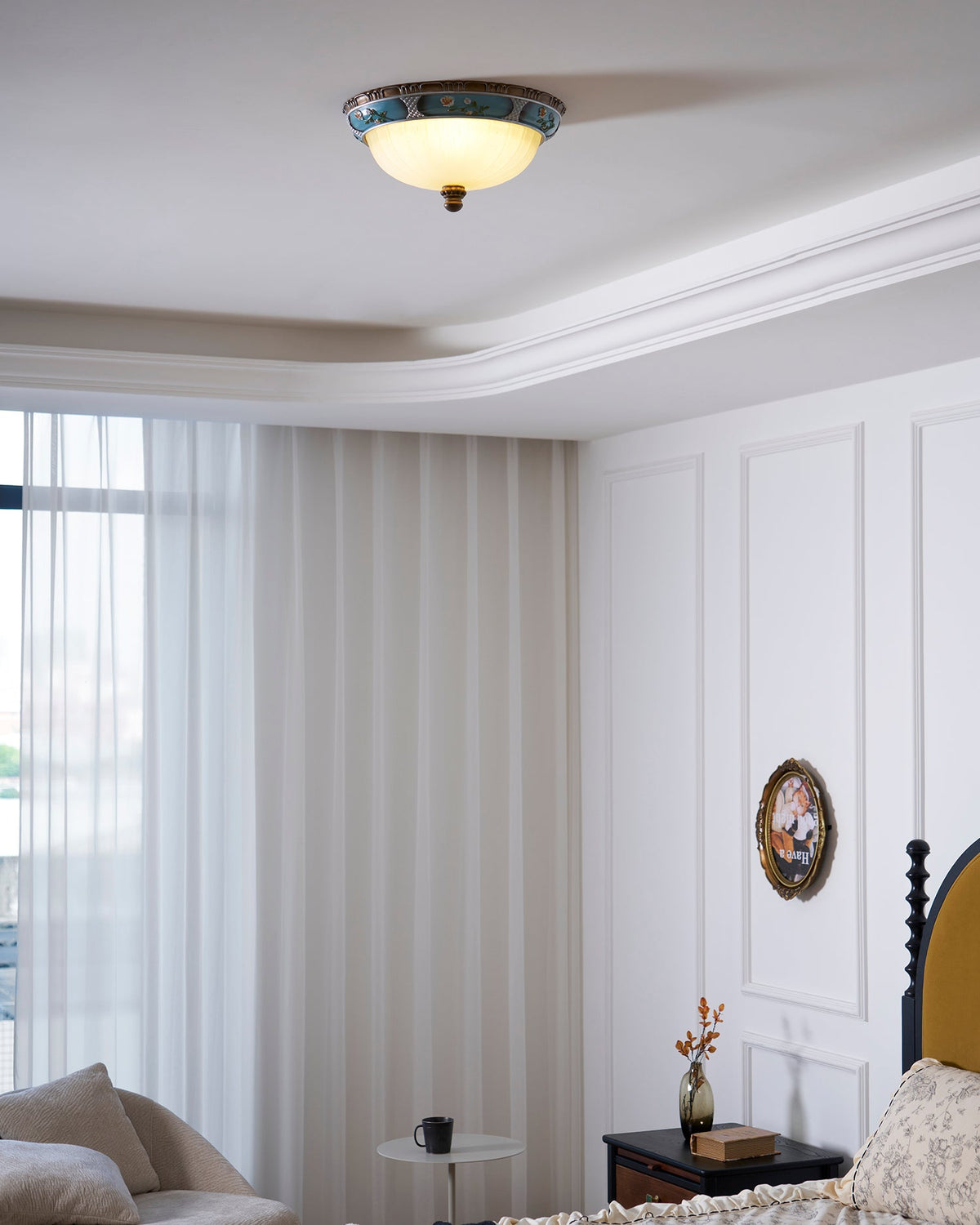 Small Clérachic ceiling light on a white ceiling with moulding, above a bedroom with sheer curtains and a panelled wall.