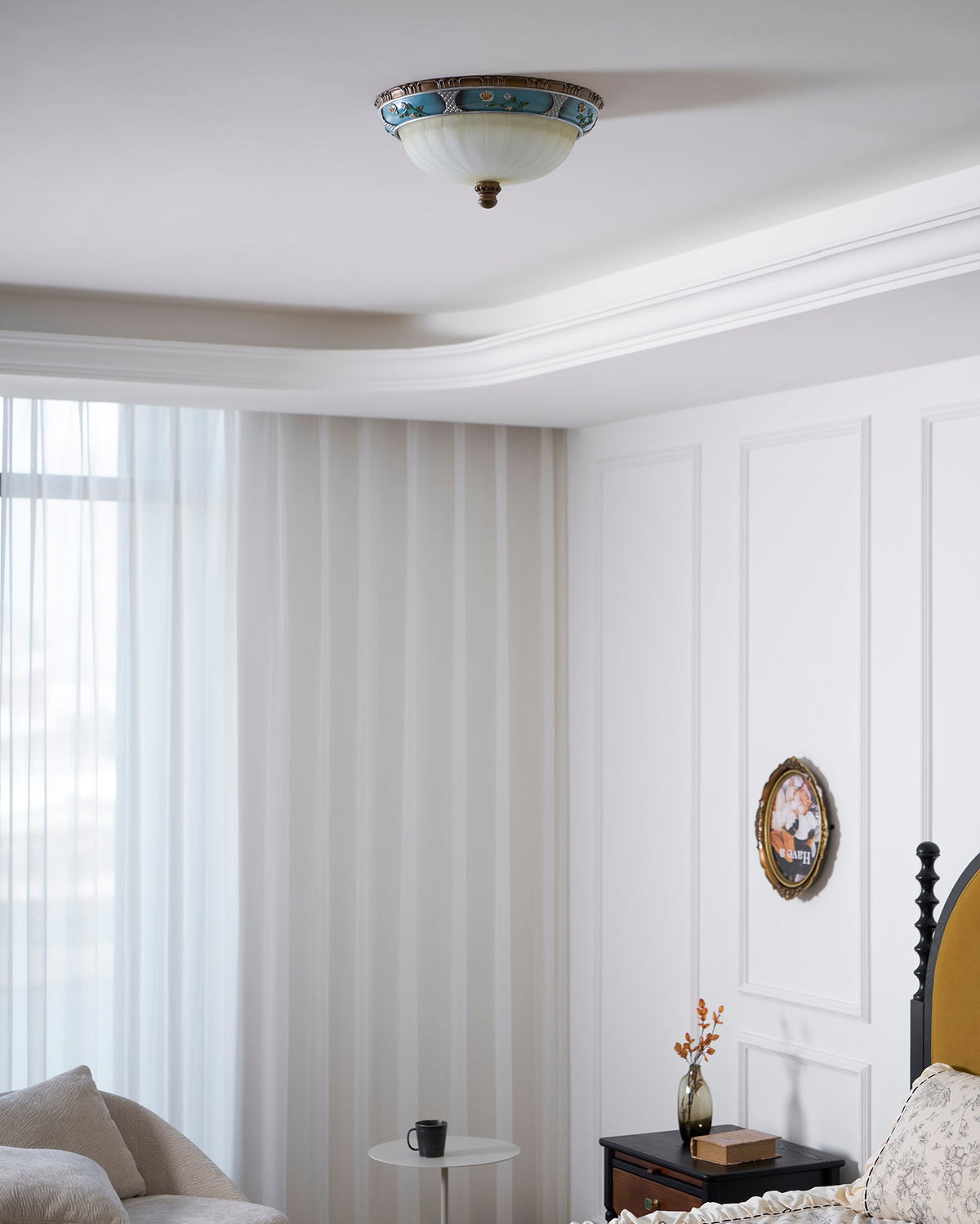 Clérachic ceiling light above a white bedroom with floor-length curtains, a panelled wall, an oval picture and a bedside table.