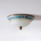 Unlit Clérachic ceiling light on a pale ceiling, its pale frosted glass bowl, turquoise floral band and brown finial all visible.