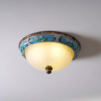 Clérachic ceiling light on a pale ceiling, lit with a warm yellow glow in its frosted glass bowl, under a turquoise floral band.