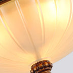Close view of the ribbed, frosted glass of this Clérachic ceiling light lit warm, with the brown finial at the bottom.