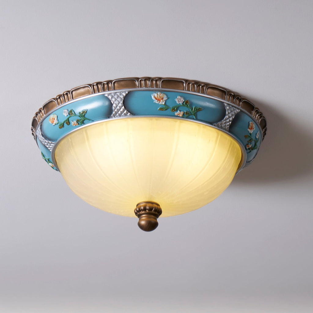 Clérachic ceiling light from a low angle, its pale yellow glass bowl lit under a turquoise floral band and brown rim.