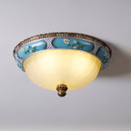 Clérachic ceiling light from a low angle, its pale yellow glass bowl lit under a turquoise floral band and brown rim.