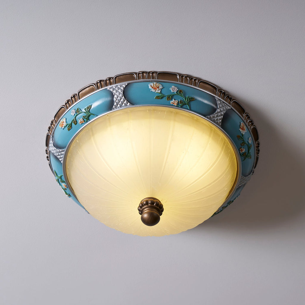 Close, low-angle view of this Clérachic ceiling light on a grey wall, the glass bowl glowing under the floral band.