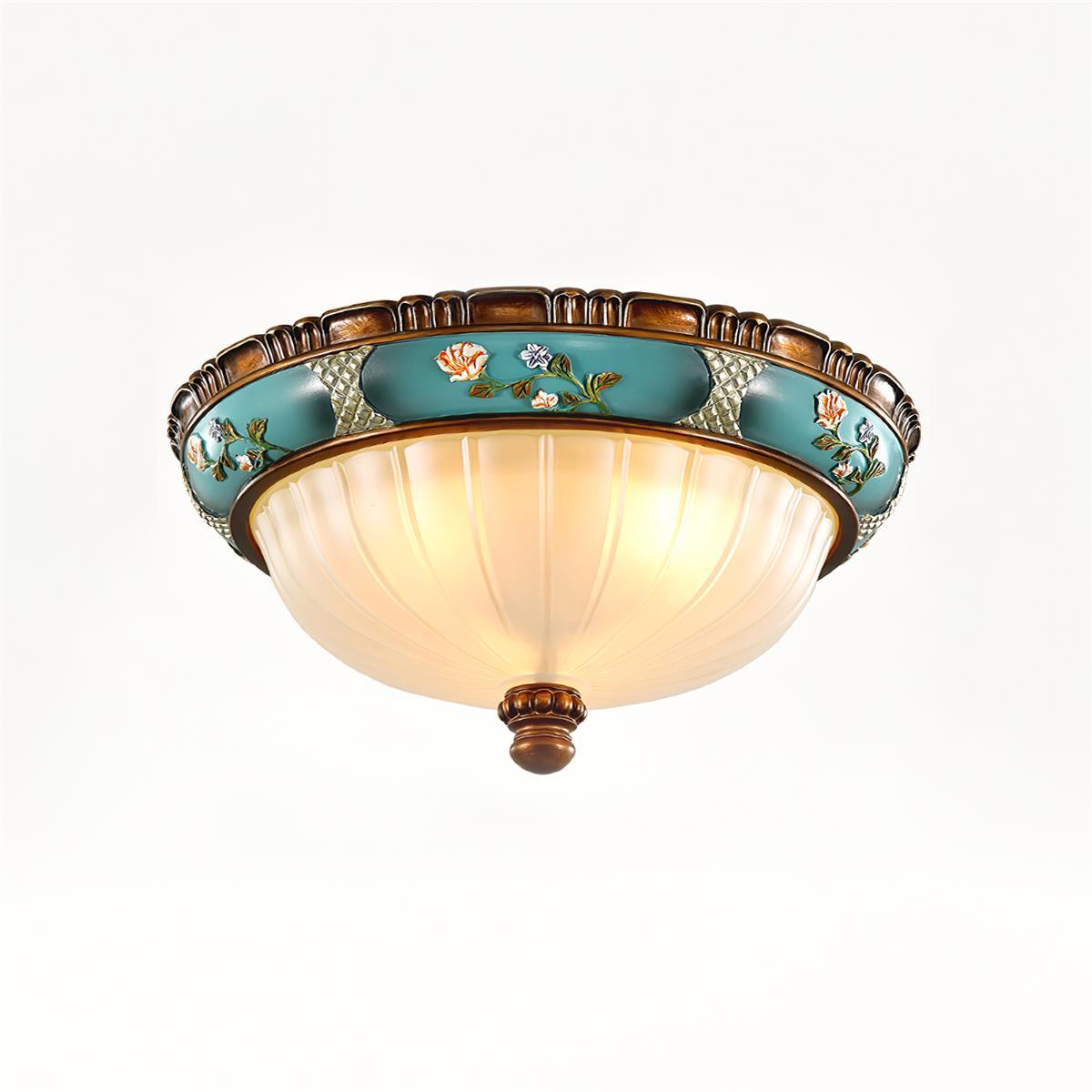 Lit Clérachic ceiling light on a white backdrop, the ribbed glass glowing warm under a turquoise band of painted flowers.