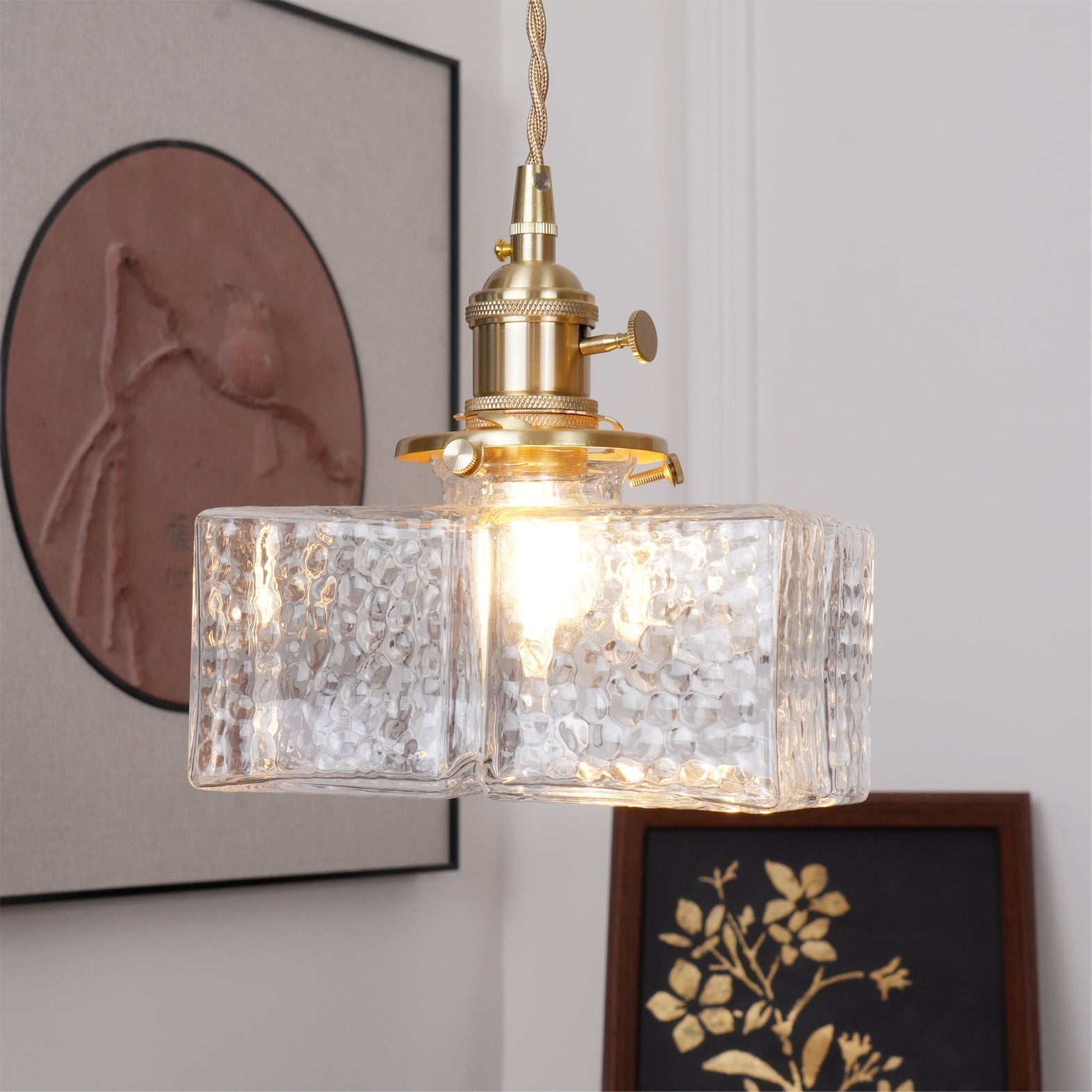 Close-up of a lit Clérachic boxy hammered-glass pendant light, Model B, with the exposed filament bulb visible inside.