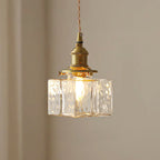 Clérachic boxy hammered-glass pendant light, Model B, lit and hanging against a plain warm taupe wall.