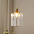 Clérachic boxy hammered-glass pendant light, tall Model C size, lit beside a curtain and a spray of white flowers.