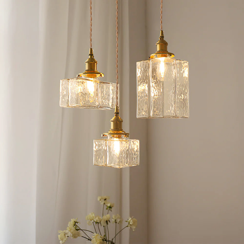Three Clérachic boxy hammered-glass pendant lights, two Model B and one Model A, lit at staggered heights near white flowers.