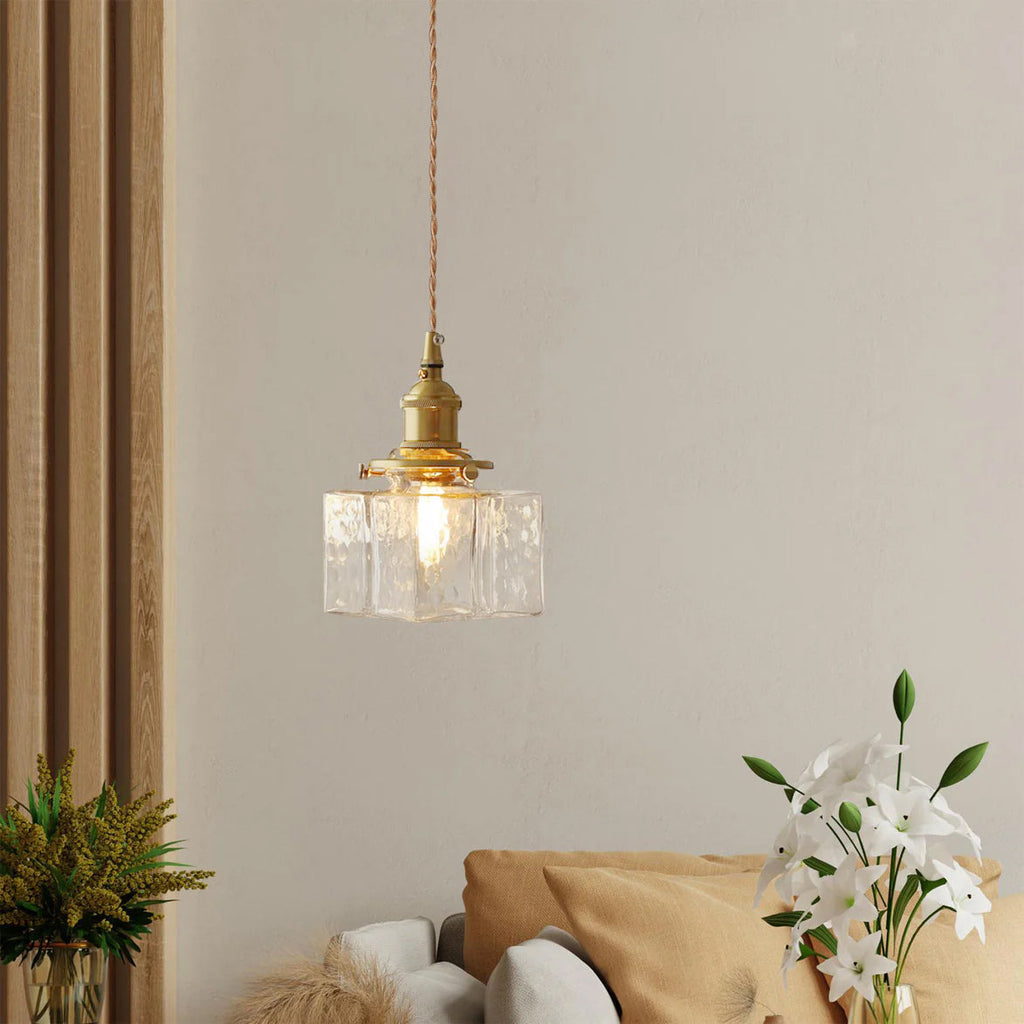 Clérachic boxy hammered-glass pendant light, Model A, lit above a beige sofa styled with white lily flowers.