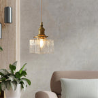 Clérachic boxy hammered-glass pendant light, Model A, lit in a living room with a textured wall and potted plant.