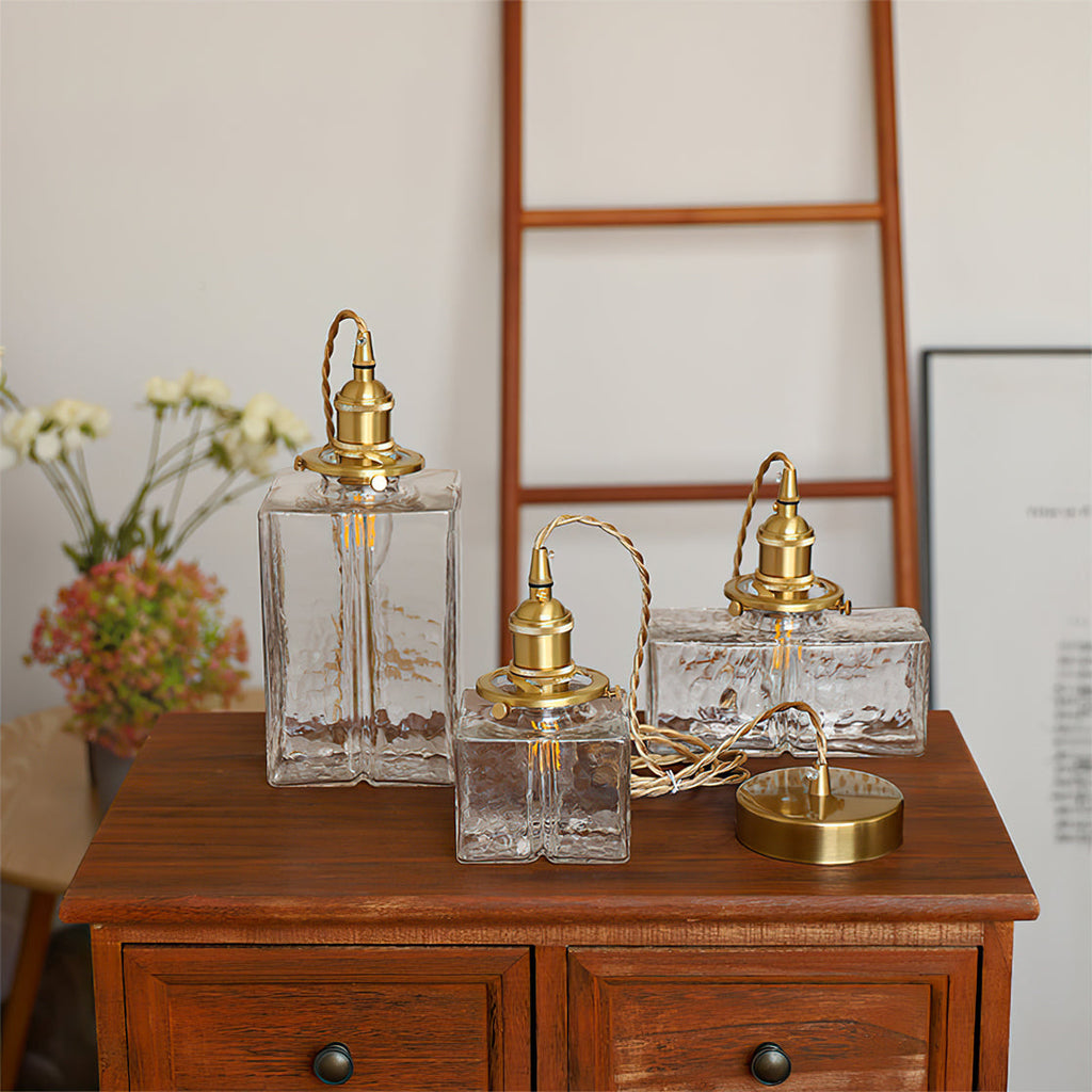 All three Clérachic boxy hammered-glass pendant light shades resting unhung on a wood dresser with the brass ceiling canopy.