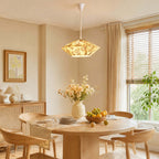 A glowing Clérachic pendant with a floral pleated shade hangs above a round oak table with a bowl of lemons and a vase of flowers.
