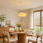 This Clérachic pendant with a glowing orange pleated shade hangs above a round table with cream chairs and spring flowers.