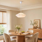 A white pleated Clérachic pendant hangs above a round oak table with cream chairs, in a room with sheer curtains.