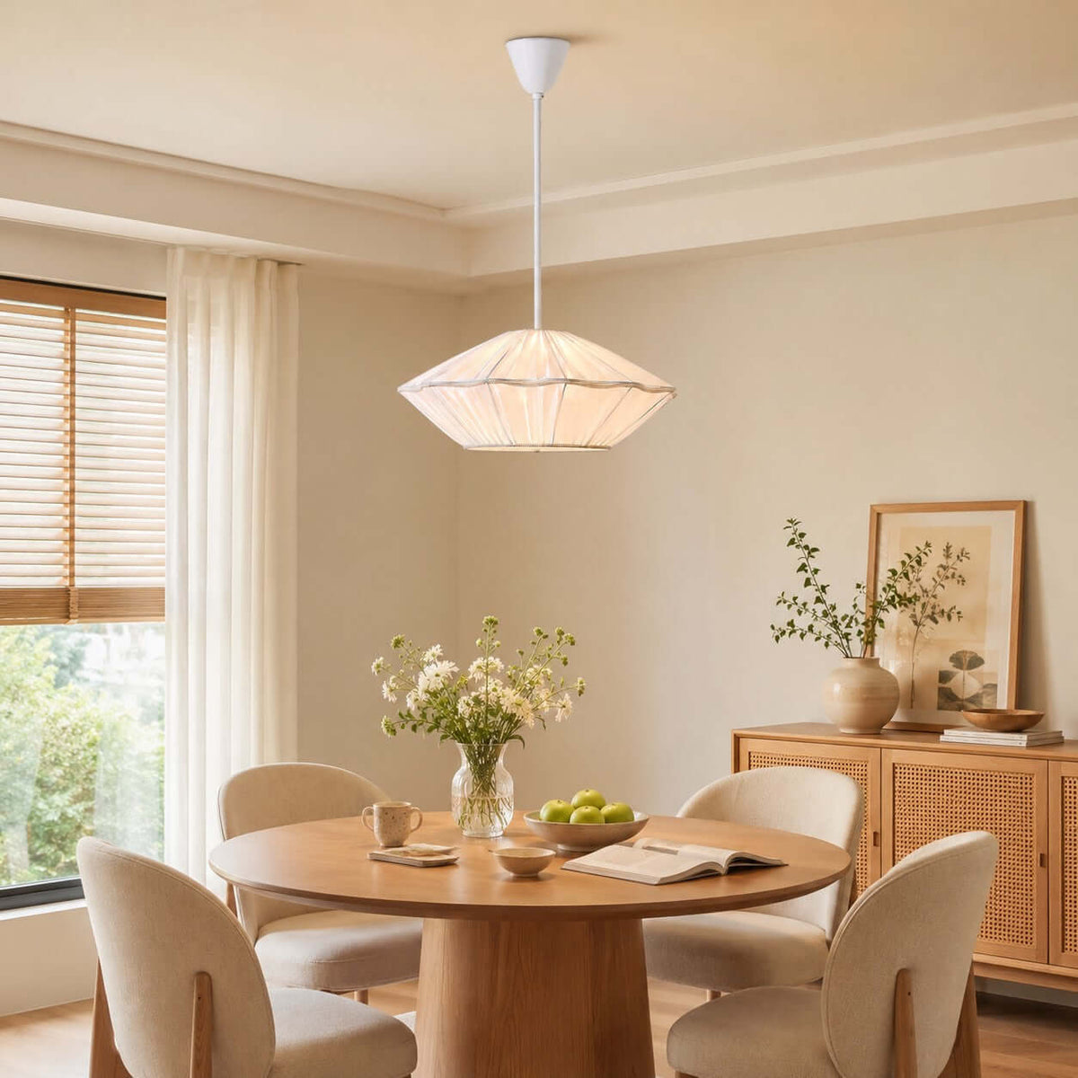 A white pleated Clérachic pendant hangs above a round oak table with cream chairs, in a room with sheer curtains.