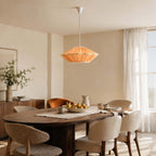 This Clérachic pendant in orange hangs over a dark oval dining table with boucle chairs and a jug of lemons.