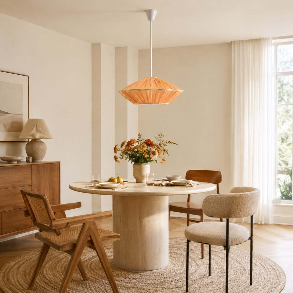 A Clérachic pendant with an orange pleated shade hangs above a pale stone round table with a jute rug beneath.