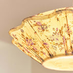 Looking up into the lit shade of this Clérachic pendant, with its scalloped trim, floral pleats and round diffuser.