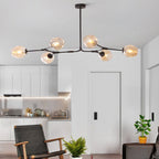 Six amber globes on the black-framed Clérachic chandelier, glowing over an open-plan kitchen and living room.