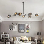 The Clérachic chandelier in smoke glass stretches across a grey living room, each globe set at its own height above the sofa.