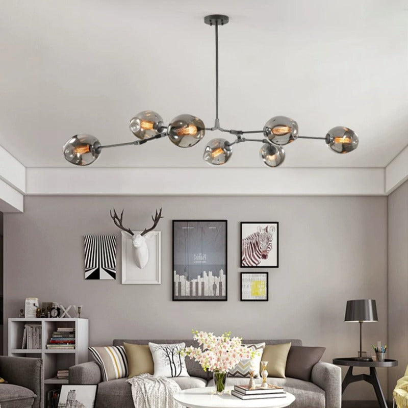 The Clérachic chandelier in smoke glass stretches across a grey living room, each globe set at its own height above the sofa.