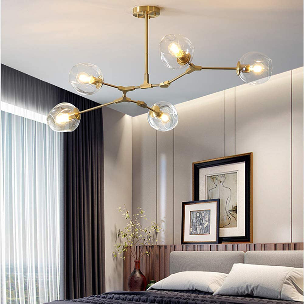 Gold-bodied Clérachic chandelier with clear dimpled globes, lit above a bedroom with framed prints and floor-length curtains.