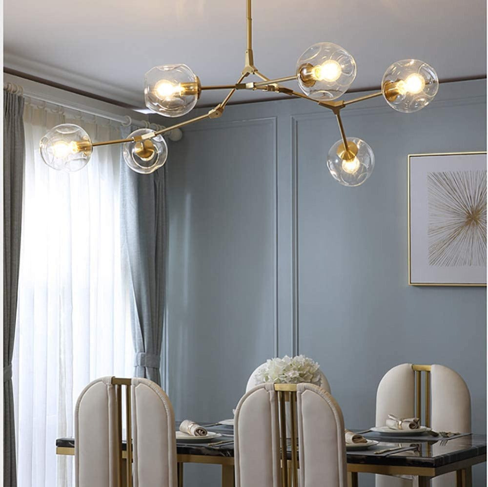 The Clérachic chandelier in gold with clear glass, hung over a marble dining table against a soft blue panelled wall.