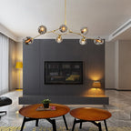 Gold-armed Clérachic chandelier with smoke globes, lit across a dark panelled media wall above two round wooden tables.