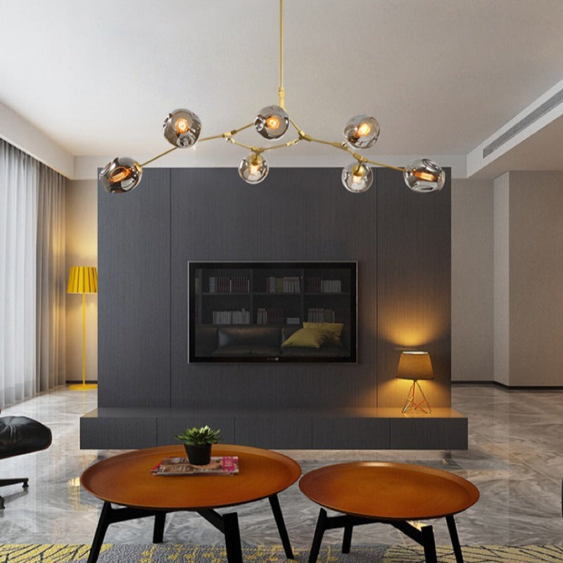 Gold-armed Clérachic chandelier with smoke globes, lit across a dark panelled media wall above two round wooden tables.