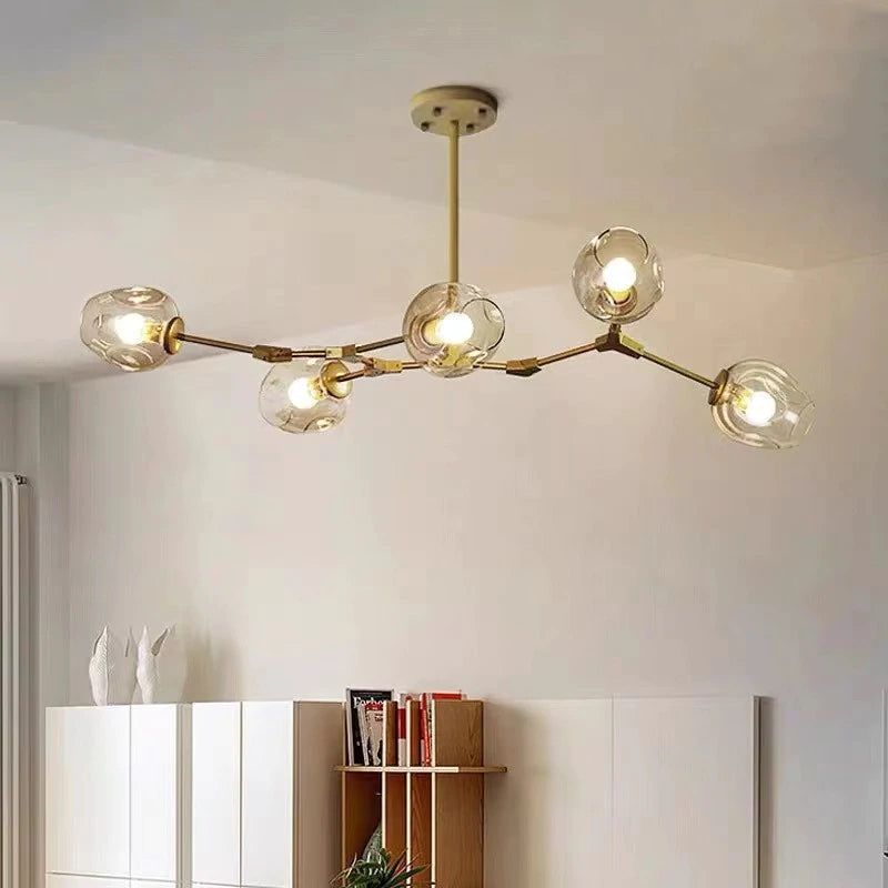 Amber globes on the gold Clérachic chandelier, lit low over white cabinetry and an open bookshelf in a pale room.