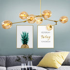 Gold Clérachic chandelier with amber globes against a teal wall, its arms crossing in front of two framed prints.