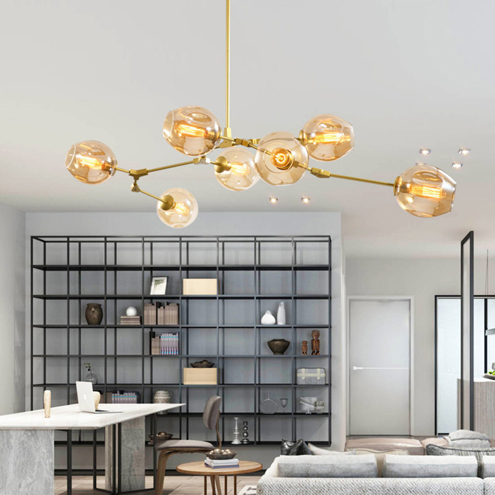 Amber-glass Clérachic chandelier on gold arms, lit above a marble counter with a black grid bookcase behind it.