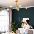 Gold Clérachic chandelier with clear dimpled globes, lit over a marble dining table against a deep green wall.