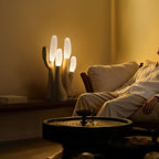 Lit beside a low daybed, this light-wood Clérachic table lamp sits on a round side table in a warm room.