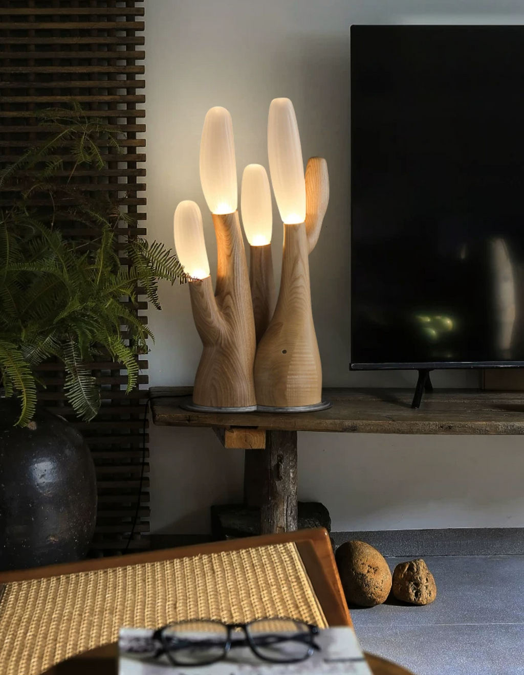 This light-wood Clérachic table lamp glows on a round side table near a television and a potted fern.