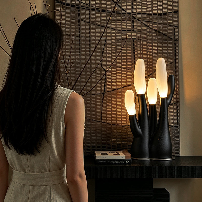 This black Clérachic table lamp lights a dark console table as a woman in linen walks toward a woven screen.