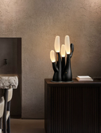 On a stone pedestal against a textured plaster wall, this black Clérachic table lamp glows softly.