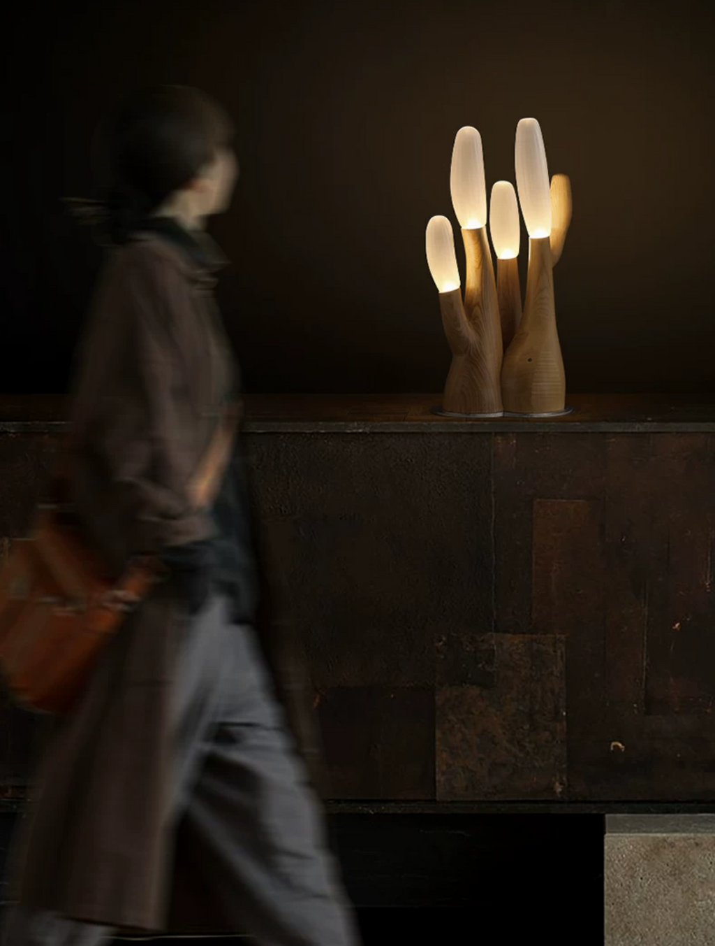 Carrying a bag over one shoulder, a blurred figure passes this light-wood Clérachic table lamp near a tiled wall.