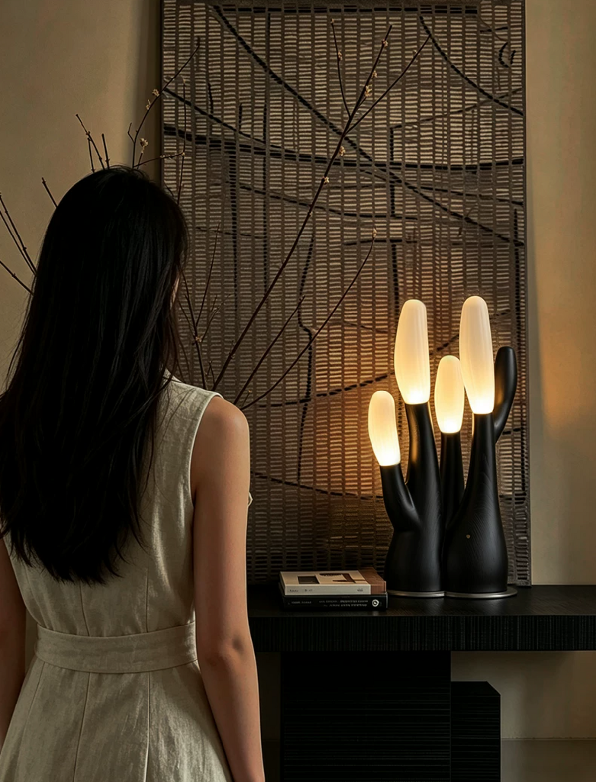 A close crop shows this black Clérachic table lamp lit on a console table near a woman in linen.