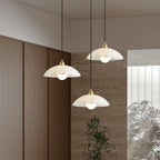 Three Clérachic alabaster pendants hung at different heights in a room with warm timber panelling, a stone wall and a leafy plant.
