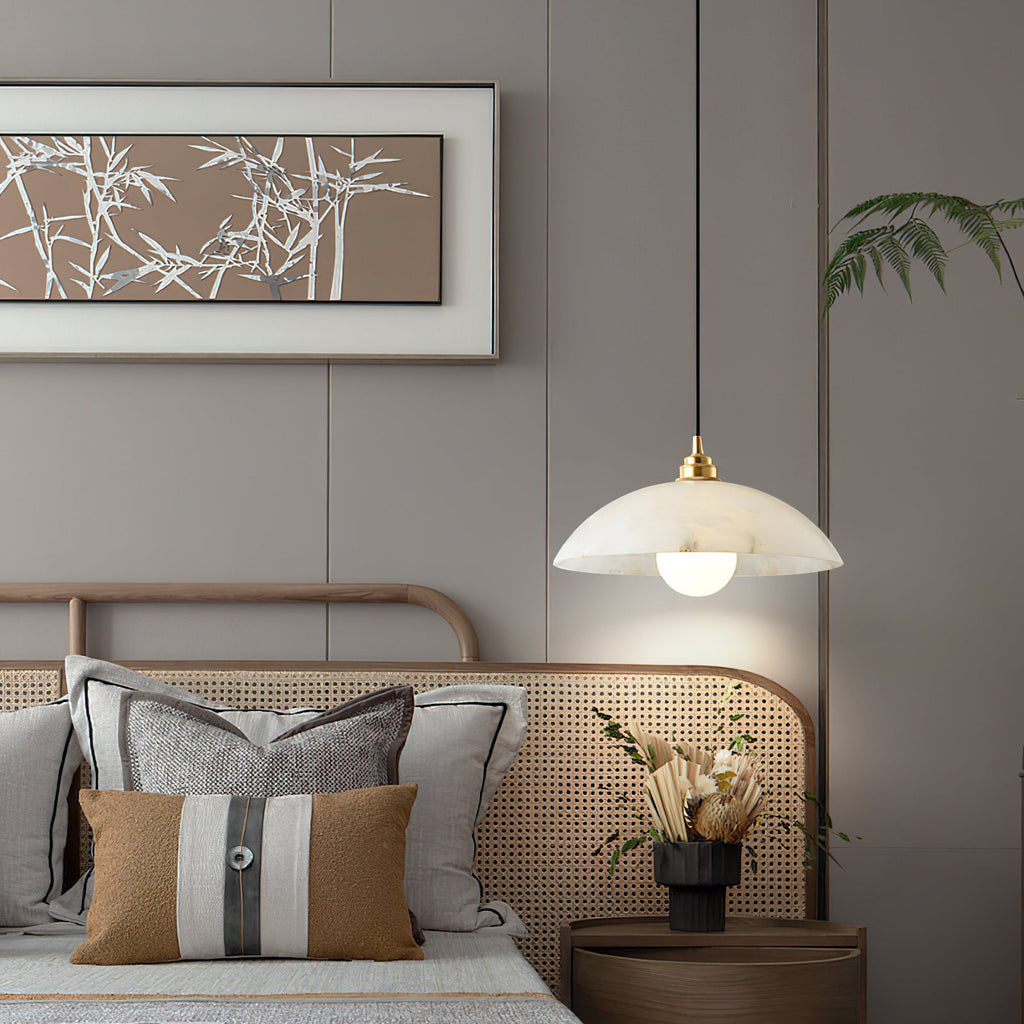 A Clérachic alabaster pendant hung beside a bed with a rattan headboard, striped cushions and a framed bamboo print above.