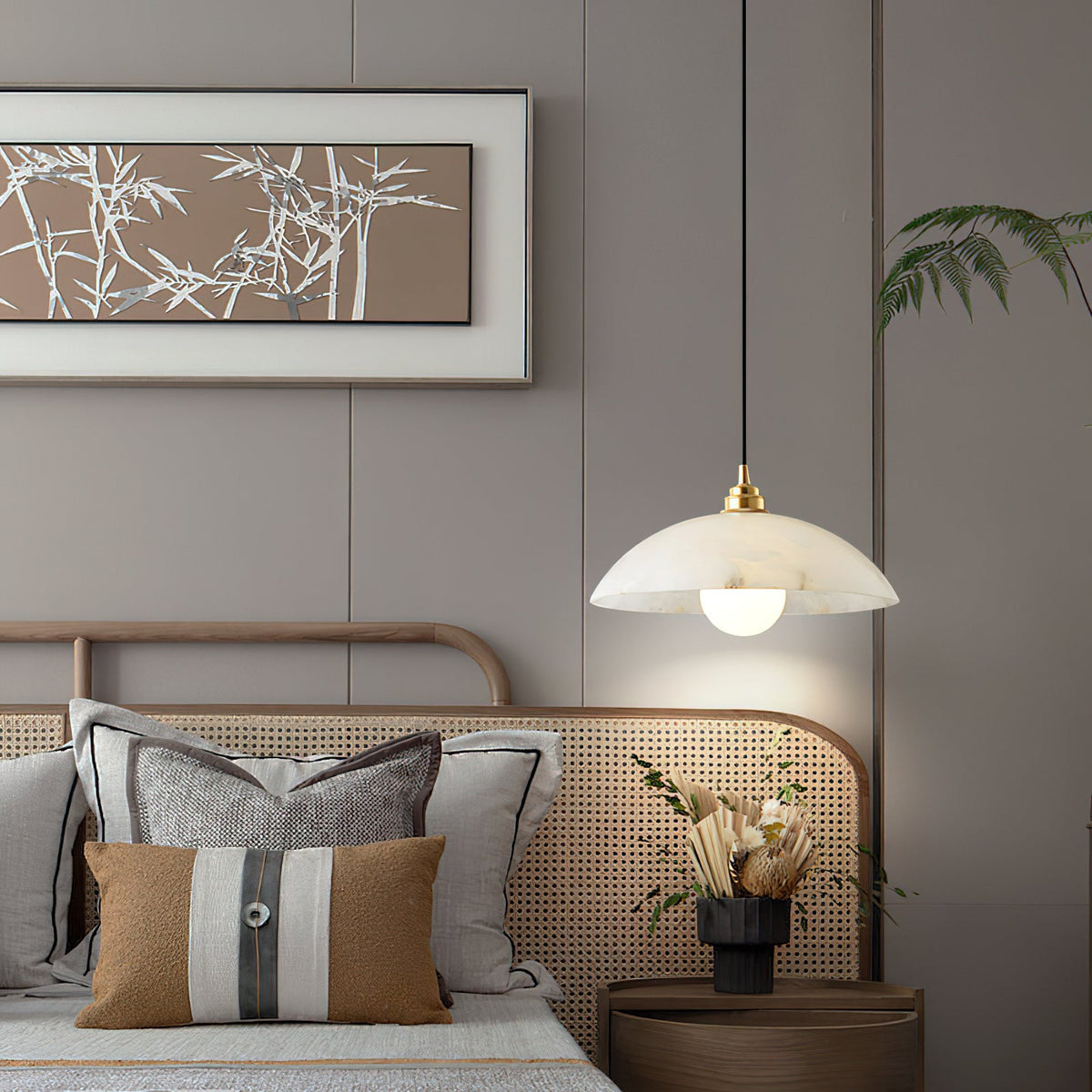 A Clérachic alabaster pendant hung beside a bed with a rattan headboard, striped cushions and a framed bamboo print above.