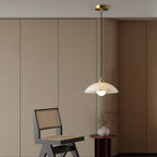 Clérachic pendant with a brass ceiling cap hanging in a room with curved cream cabinetry, a cane chair and a small vase on a round side table.