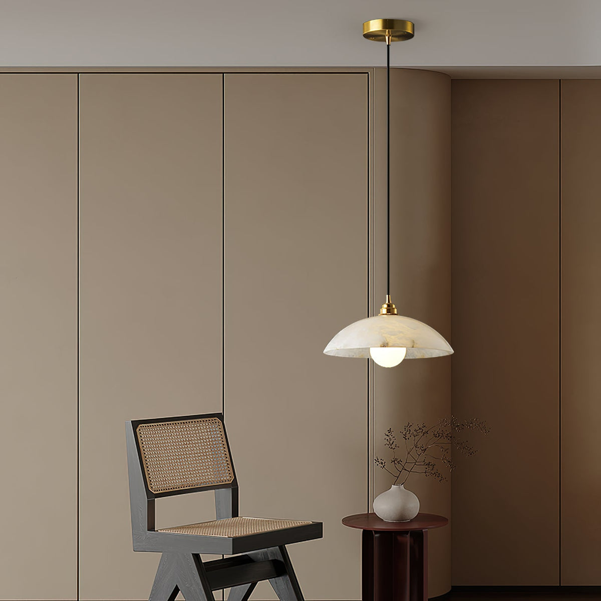 Clérachic pendant with a brass ceiling cap hanging in a room with curved cream cabinetry, a cane chair and a small vase on a round side table.